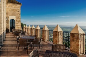 Una terraza al aire libre con paredes de piedra, mesas y sillas, con vistas a un paisaje pintoresco.