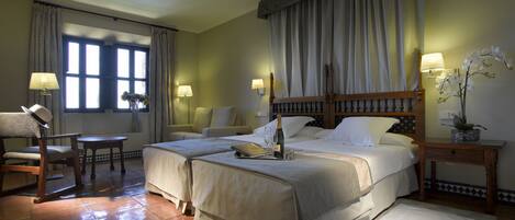 Une chambre d’hôtel avec un grand lit, deux tables de chevet, une chaise, une petite table et une fenêtre avec des rideaux.