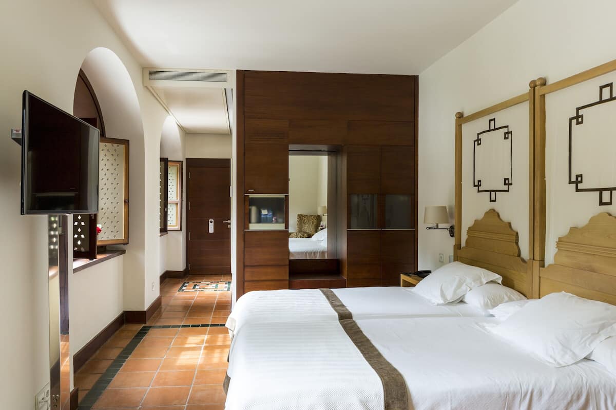 Quarto de hotel com uma cama grande, televisão, cabeceira de madeira e espelho na parede.