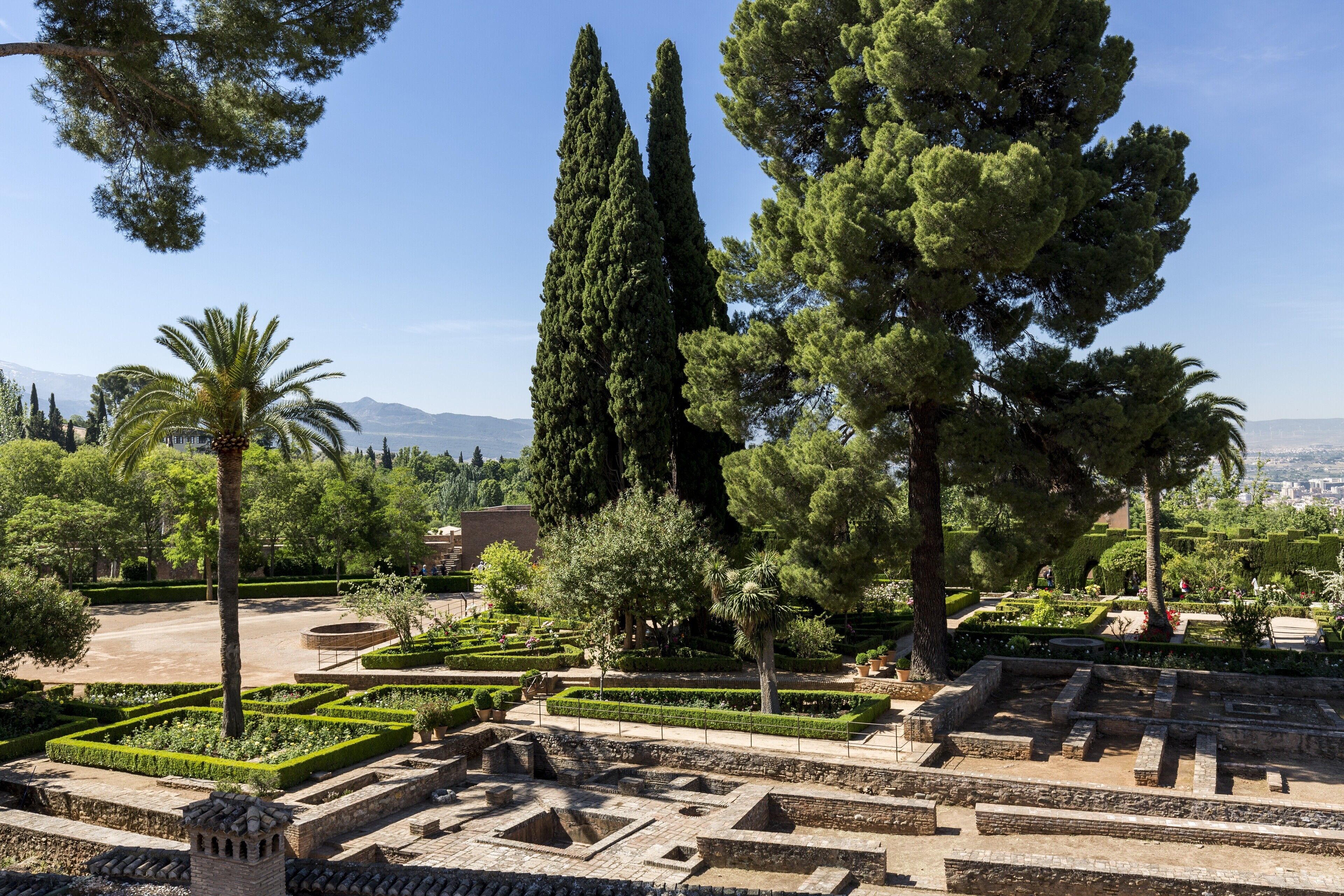 A historical site with well-maintained gardens, tall cypress trees, and ancient ruins.