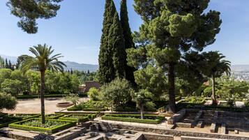 A historical site with well-maintained gardens, tall cypress trees, and ancient ruins.