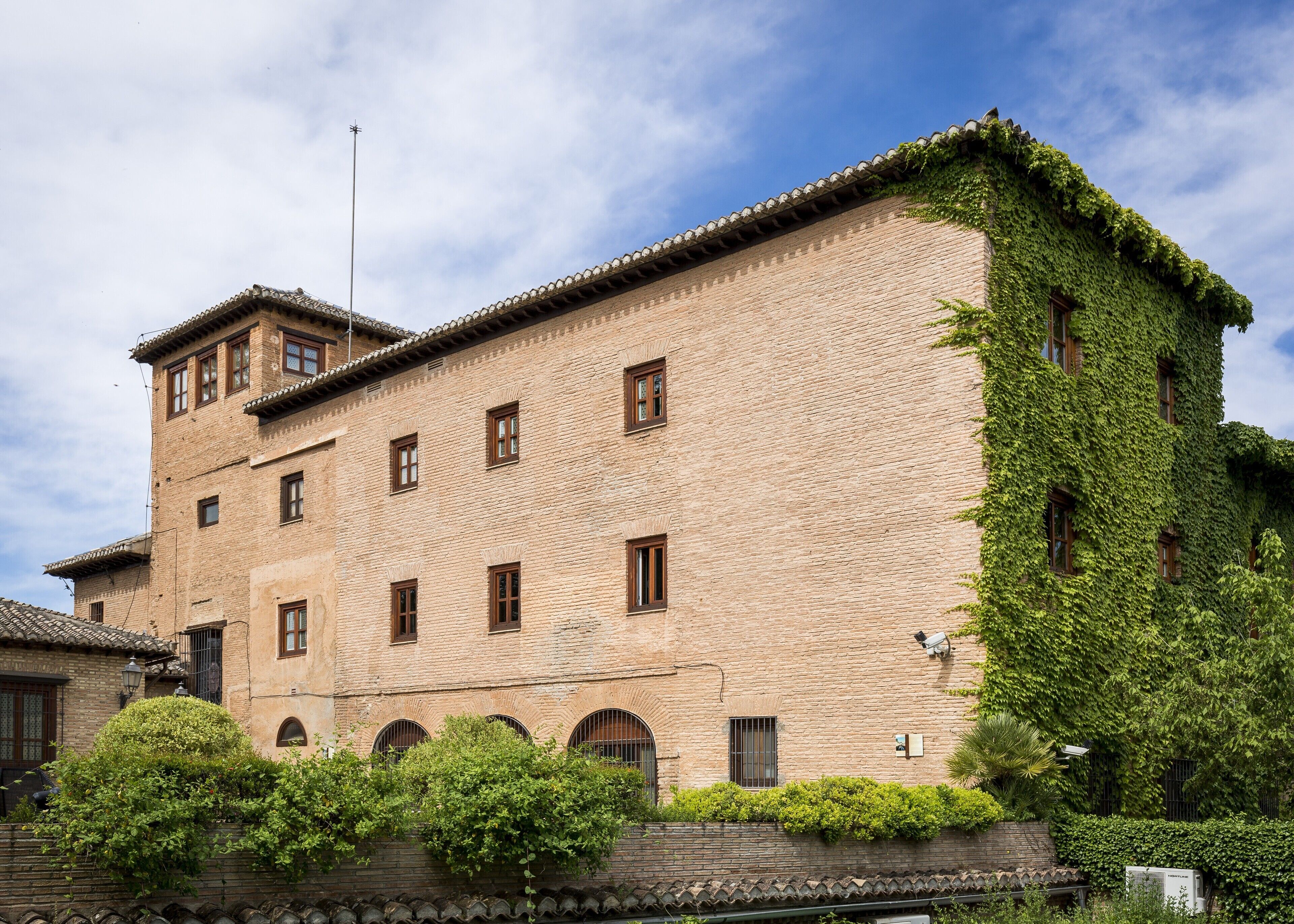 Un edificio histórico con fachada de ladrillo, varias ventanas y una sección cubierta de hiedra.