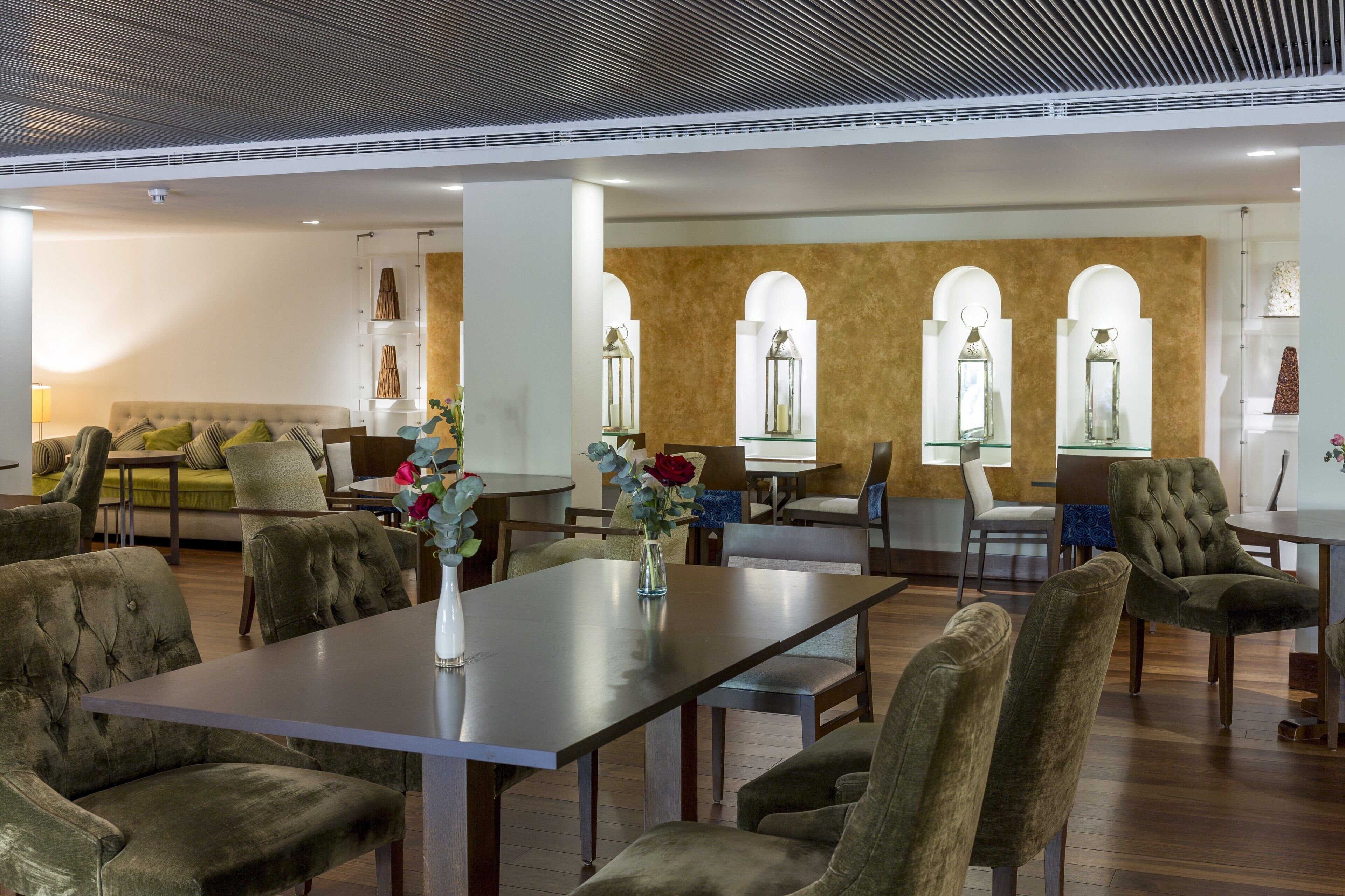 Un moderno vestíbulo de hotel con zona de comedor central, asientos cómodos y jarrones de cristal decorativos.