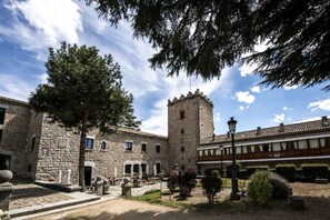 A courtyard with stone buildings, a tower, and outdoor seating. - Parador De Avila (Ávila)