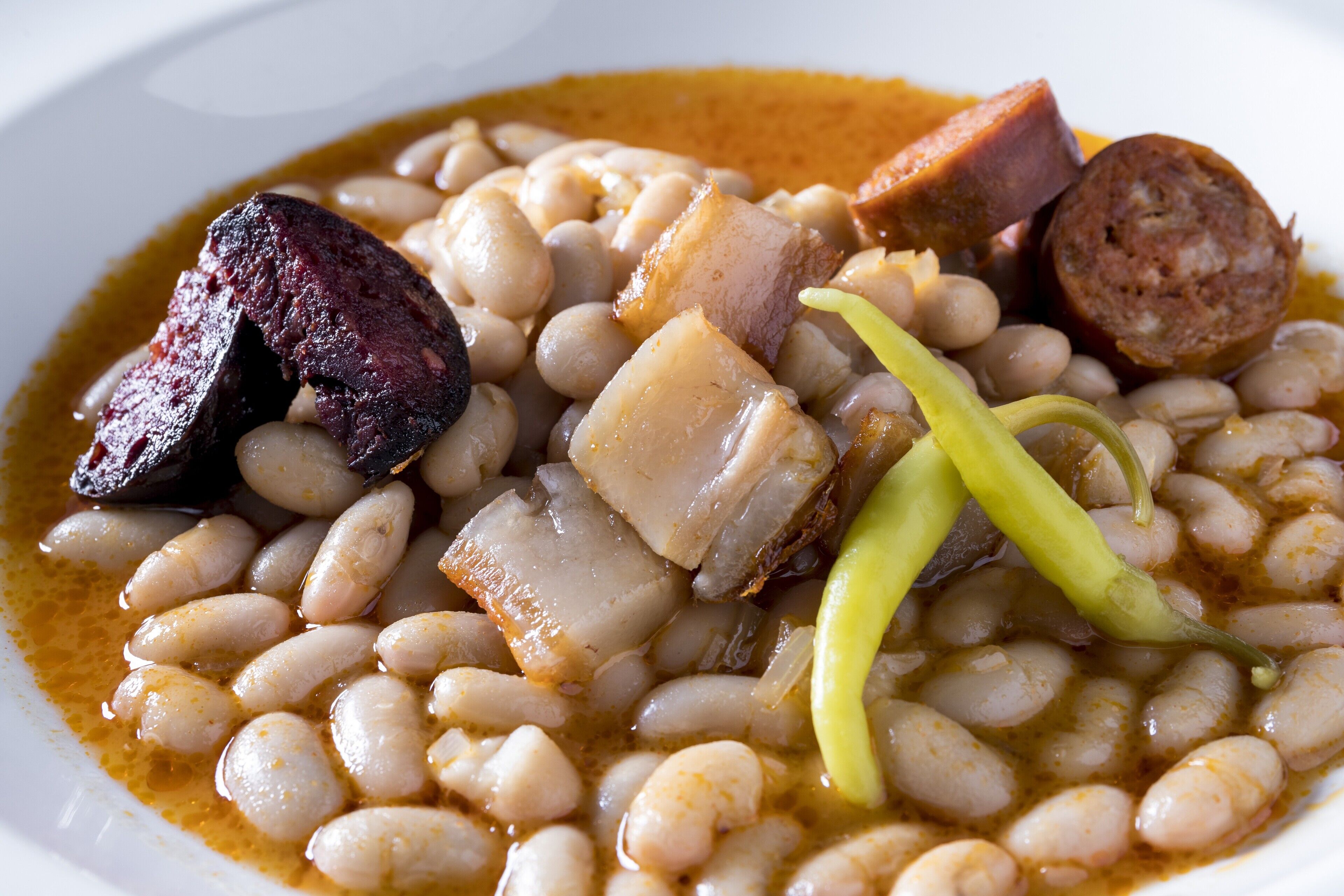 Un piatto con fagioli, salsiccia e pezzi di carne.
