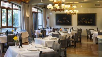 A restaurant with multiple tables set for dining, large windows, and chandeliers.