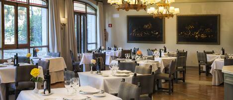 A restaurant with multiple tables set for dining, large windows, and chandeliers.