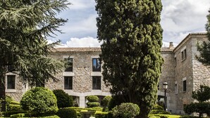Un edificio de piedra con un sendero de jardín que lleva a un alto árbol de hoja perenne.