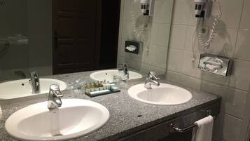 A bathroom with two sinks, a mirror, a towel rack, and a hairdryer mounted on the wall.