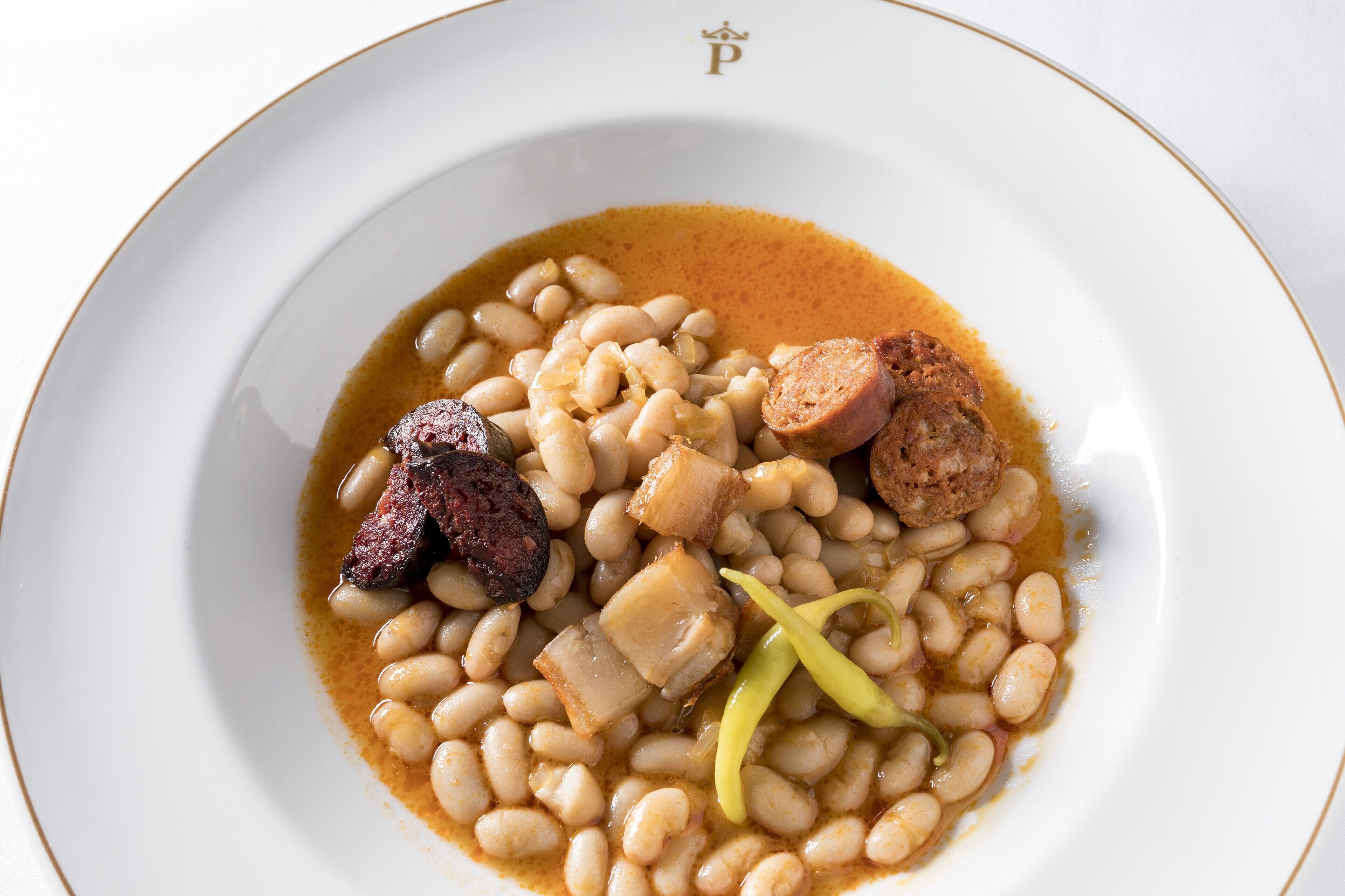 Une assiette de haricots avec des saucisses et une tranche de viande.