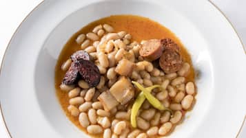 Une assiette de haricots avec des saucisses et une tranche de viande.