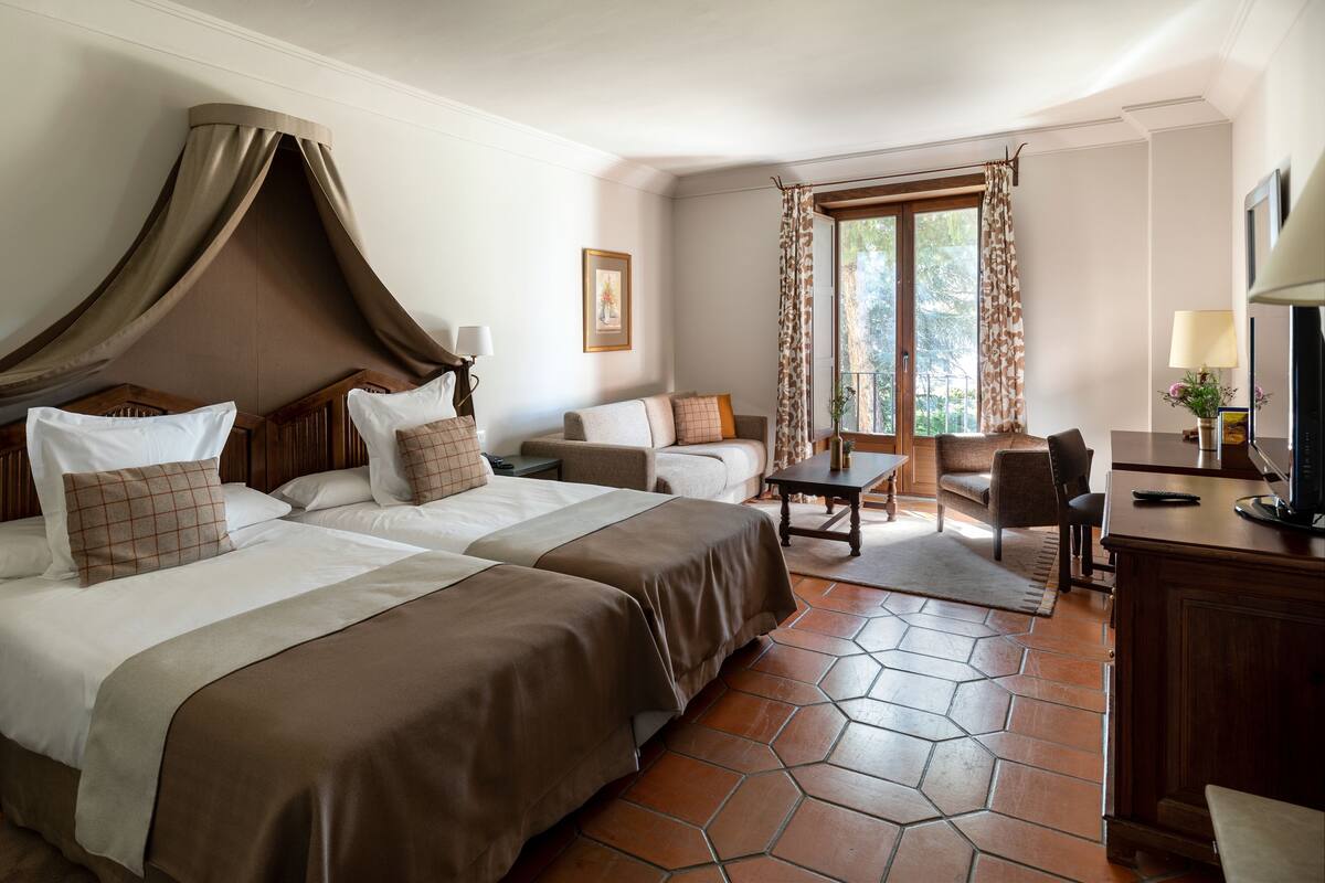 Habitación de hotel con dos camas, un escritorio, una silla y una ventana con cortinas.