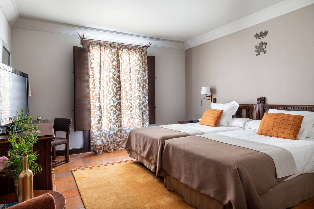 Habitación de hotel con dos camas, un escritorio, una silla, un televisor y una ventana con cortinas.