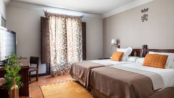 Ein Hotelzimmer mit zwei Betten, einem Schreibtisch, einem Stuhl, einem Fernseher und einem Fenster mit Vorhängen.