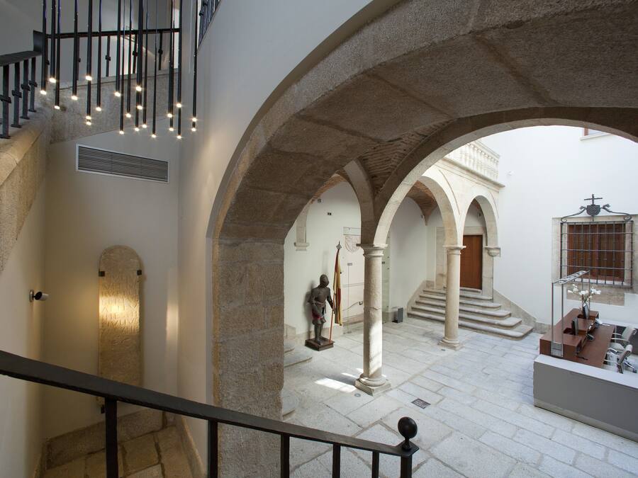 Un interior espacioso con una escalera, columnas de piedra y un mostrador de recepción.