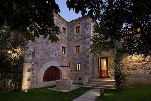 Un edificio de piedra con patio central, una fuente y una escalera hacia la entrada.