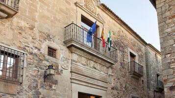 Un bâtiment historique en pierre, doté d’un balcon orné de drapeaux, une rue pavée et un sentier bordé de pierres.