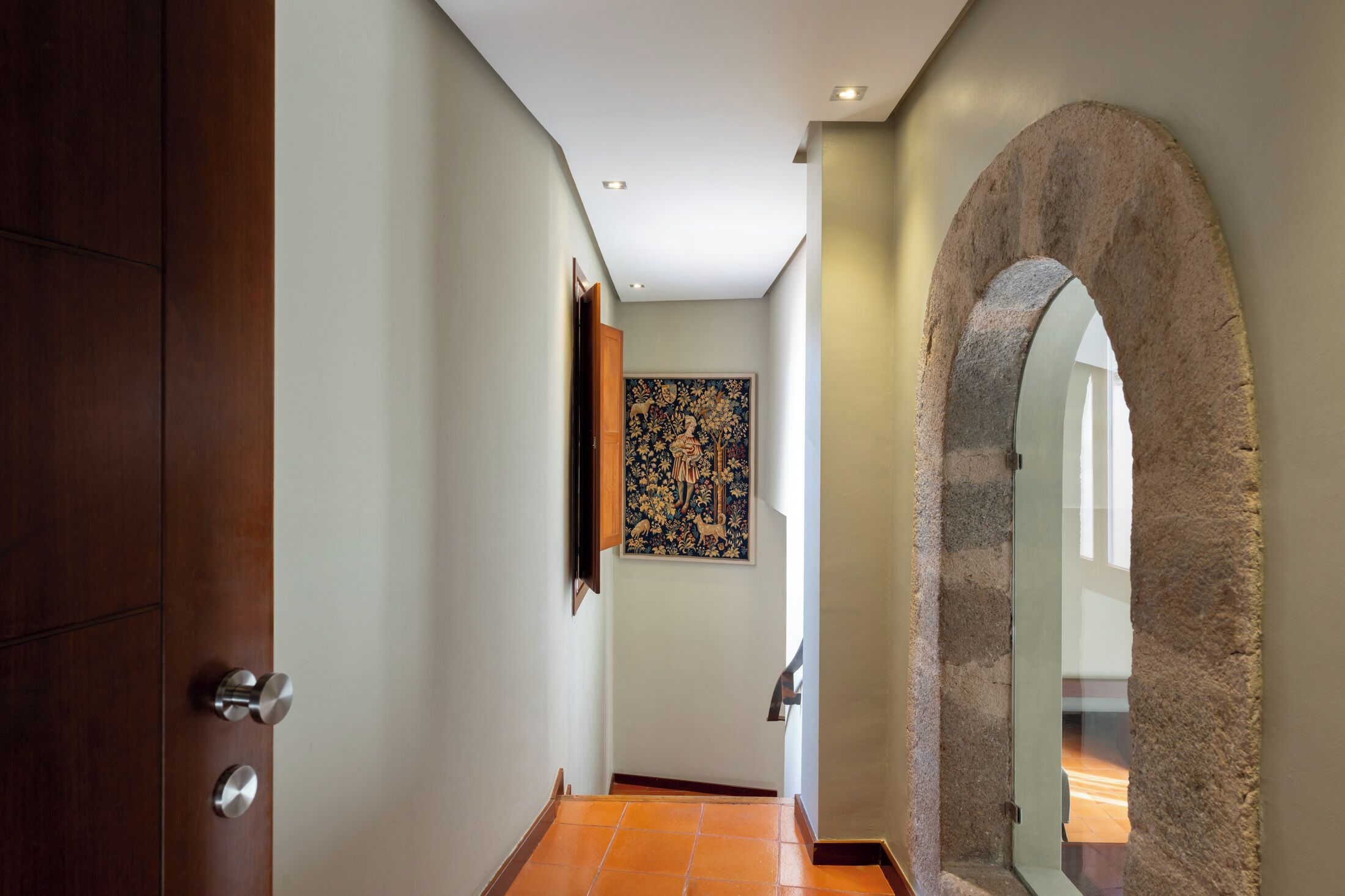 Un pasillo con una puerta de madera, un arco de piedra y una obra de arte enmarcada en la pared.