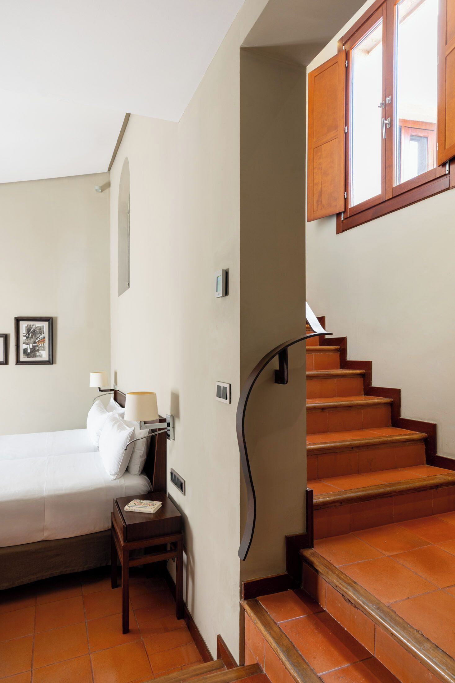Un dormitorio con cama, mesita de noche, lámpara y una escalera de madera con escalones y barandilla.