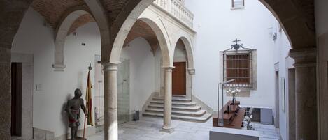 Ein Innenhof mit Steinbögen, einer Statue und einer Treppe, die zu einer oberen Ebene führt.