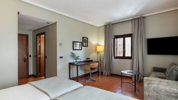Een hotelkamer met een bed, bureau, stoel, bank, televisie en raam met gordijnen.