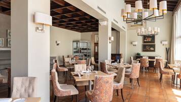 Un restaurante con varias mesas y sillas, suelo de baldosas e iluminación colgante.
