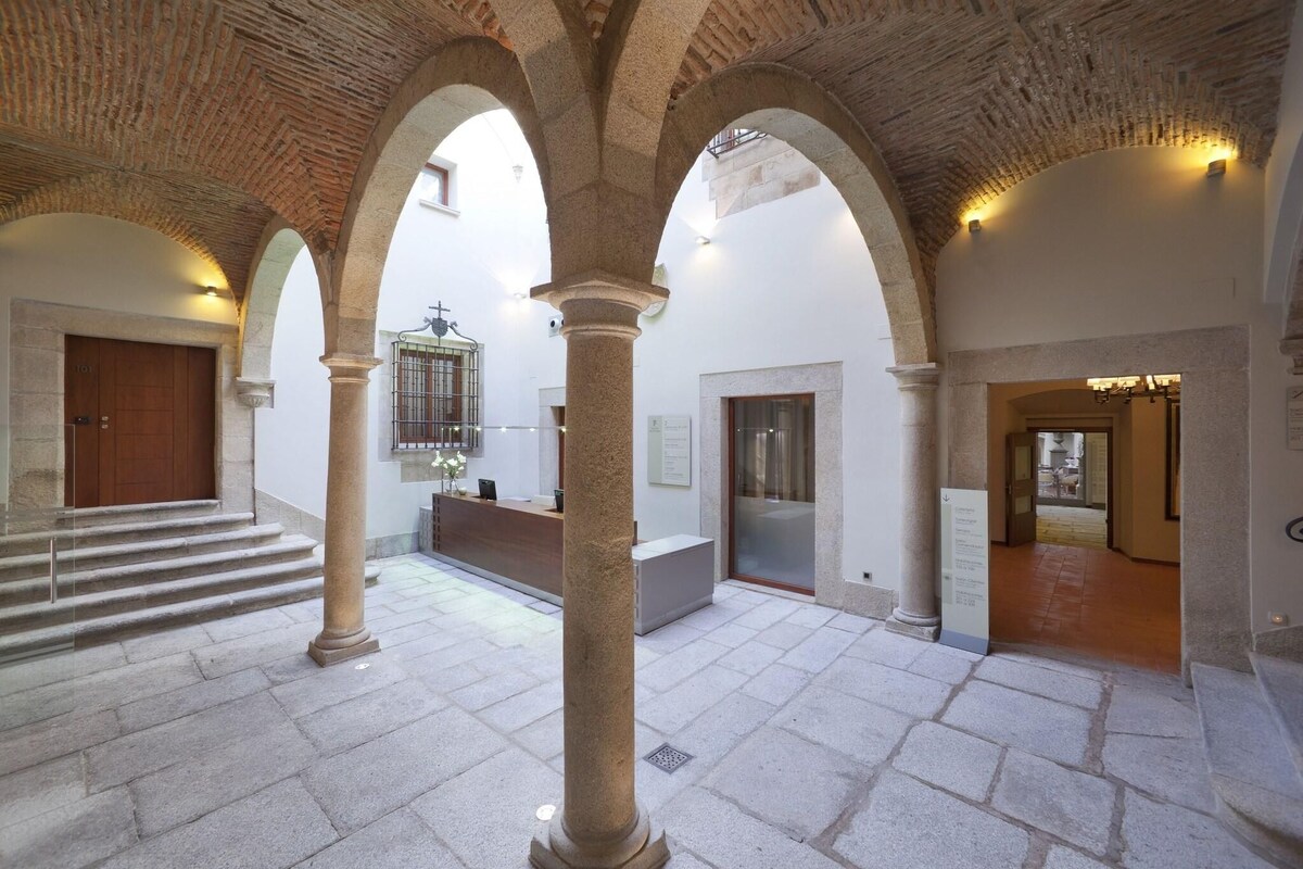 A spacious interior with stone columns, a wooden door, and a staircase leading to an upper level.