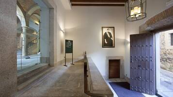 A hallway with stone steps, a framed portrait on the wall, a wooden door with metal studs, and a staircase visible through a glass door.