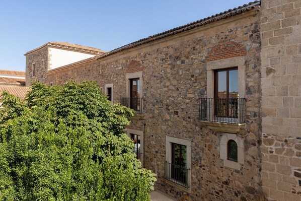 Un edificio de piedra con balcones y ventanas, rodeado de vegetación.