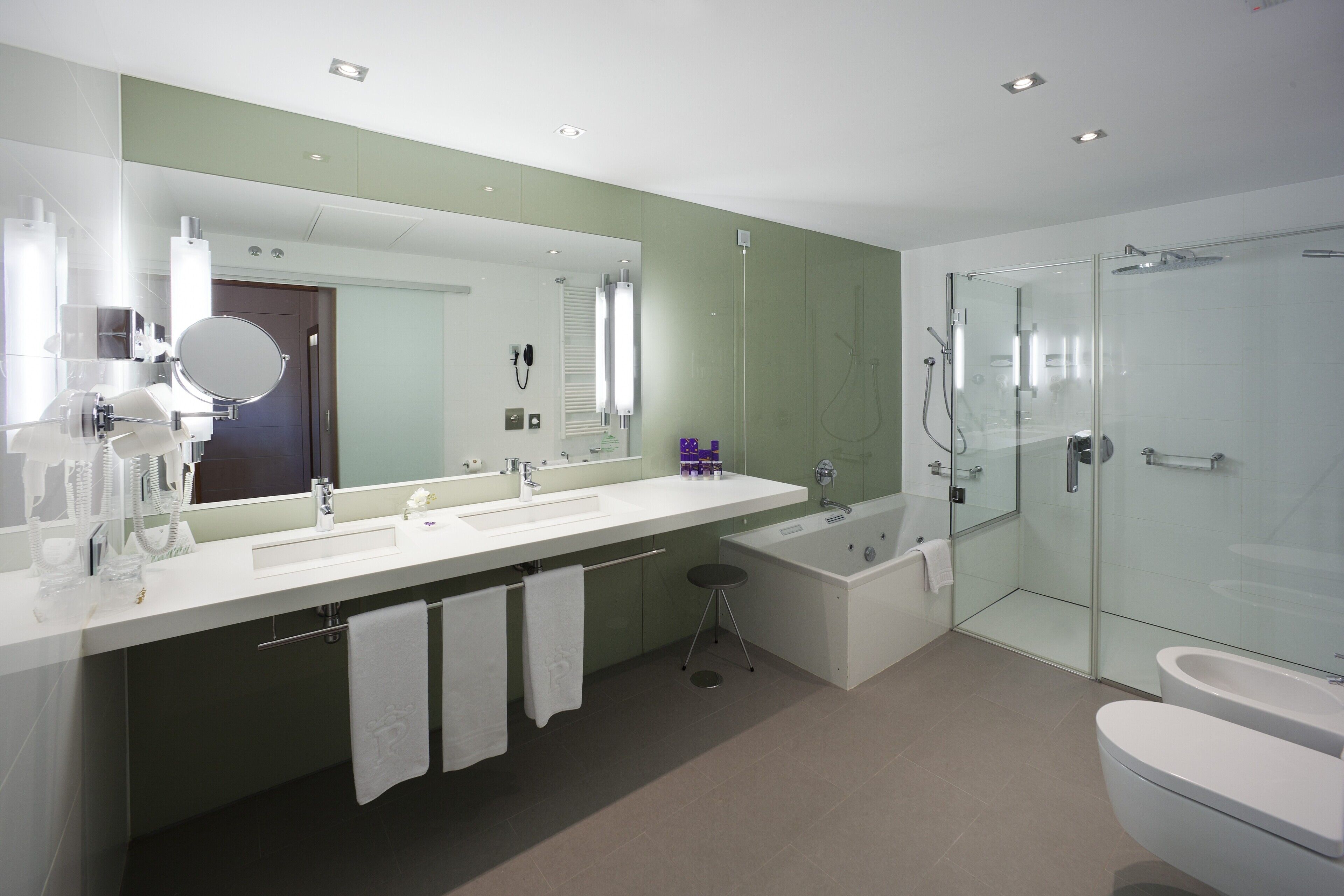 Een moderne badkamer met een grote spiegel, twee wasbakken, een badkuip en een douche met glazen wanden.