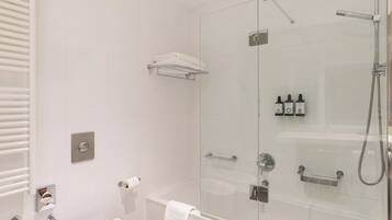 Un baño moderno con ducha de vidrio, inodoro blanco, barra para toallas y estante con artículos de aseo.