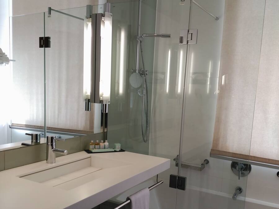 Un baño moderno con ducha envuelta en vidrio, un espejo grande y un lavabo blanco con toallero.