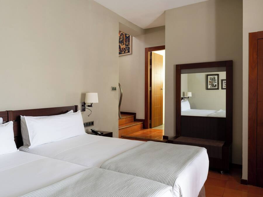 A hotel room with two beds, a nightstand, a lamp, a mirror, and a wooden door.