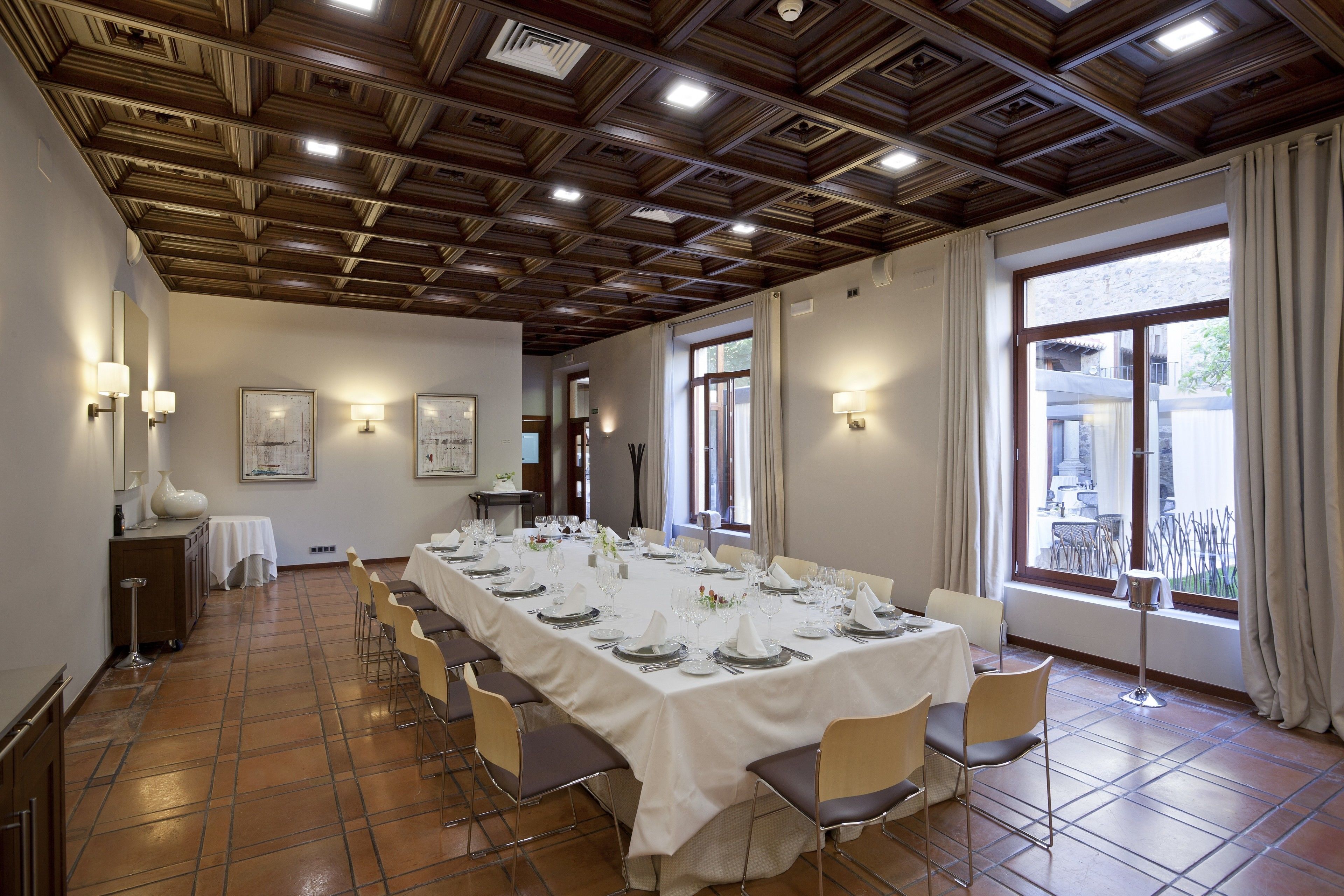 A conference room with a long table set for a meeting, wooden ceiling, and large windows with curtains.