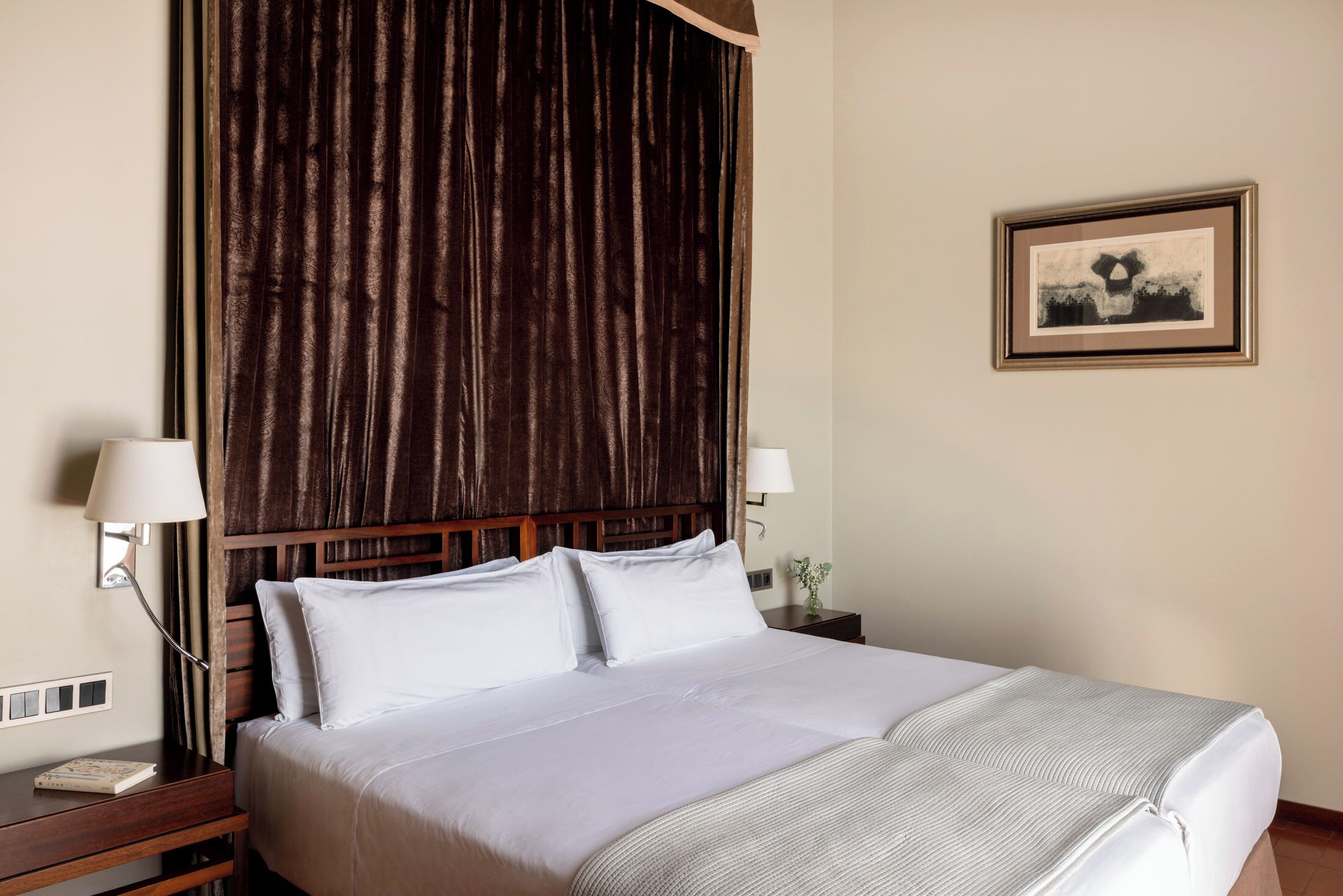 Une chambre d’hôtel avec un grand lit, deux tables de chevet, une tête de lit et un tableau encadré au mur.