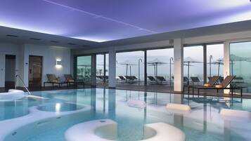 An indoor swimming pool with lounge chairs and a view of the city skyline.