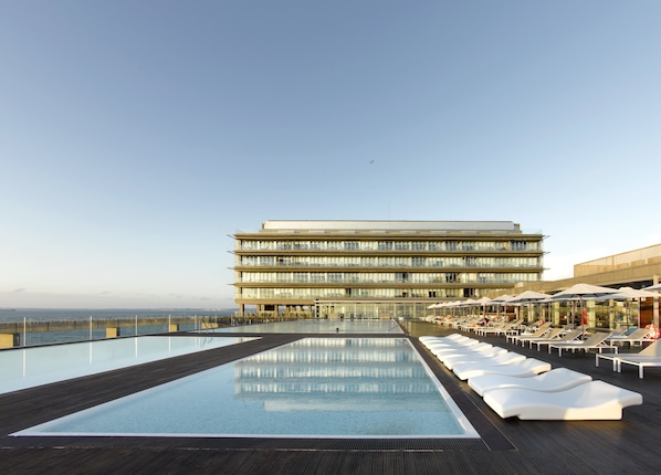 A modern hotel with a rooftop infinity pool, lounge chairs, and a view of the sea. - Parador De Cadiz (Cádiz)
