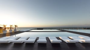 Zona junto a la piscina con tumbonas y plantas en macetas, con vista a un cuerpo de agua.