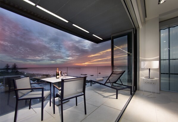 A modern outdoor seating area with a table and chairs, overlooking a scenic sunset view.