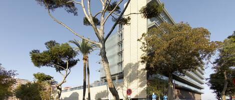 Un edificio moderno con un diseño angular distintivo, rodeado de árboles y un cielo despejado.