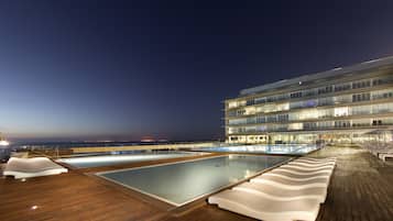 Un área de piscina con dos piscinas, sillas de descanso y un edificio de varios pisos y balcones.