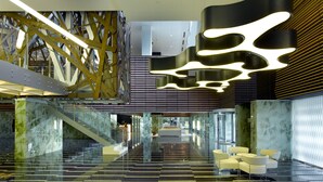 Eine moderne Lobby mit einer Glasstiege, einer zentralen Sitzgruppe und einem außergewöhnlichen Deckenstil.