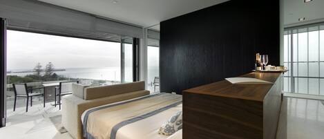 Un dormitorio moderno con una cama grande, un escritorio de madera y un balcón con vistas al mar.