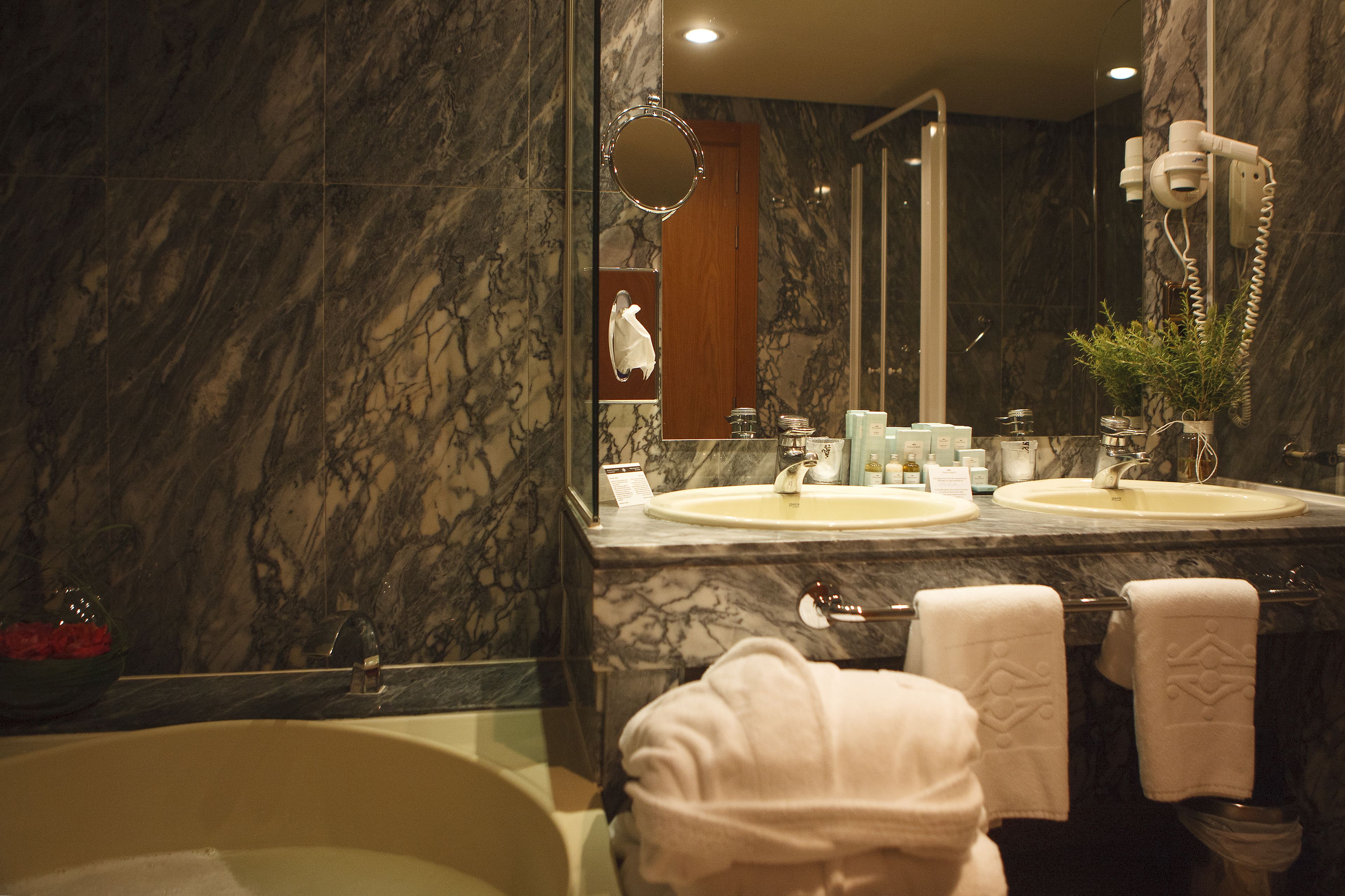Une salle de bain avec des murs en marbre, deux lavabos, une baignoire et un miroir.