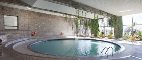 An indoor swimming pool with a brick wall, a lifebuoy, and a view of the outdoors.