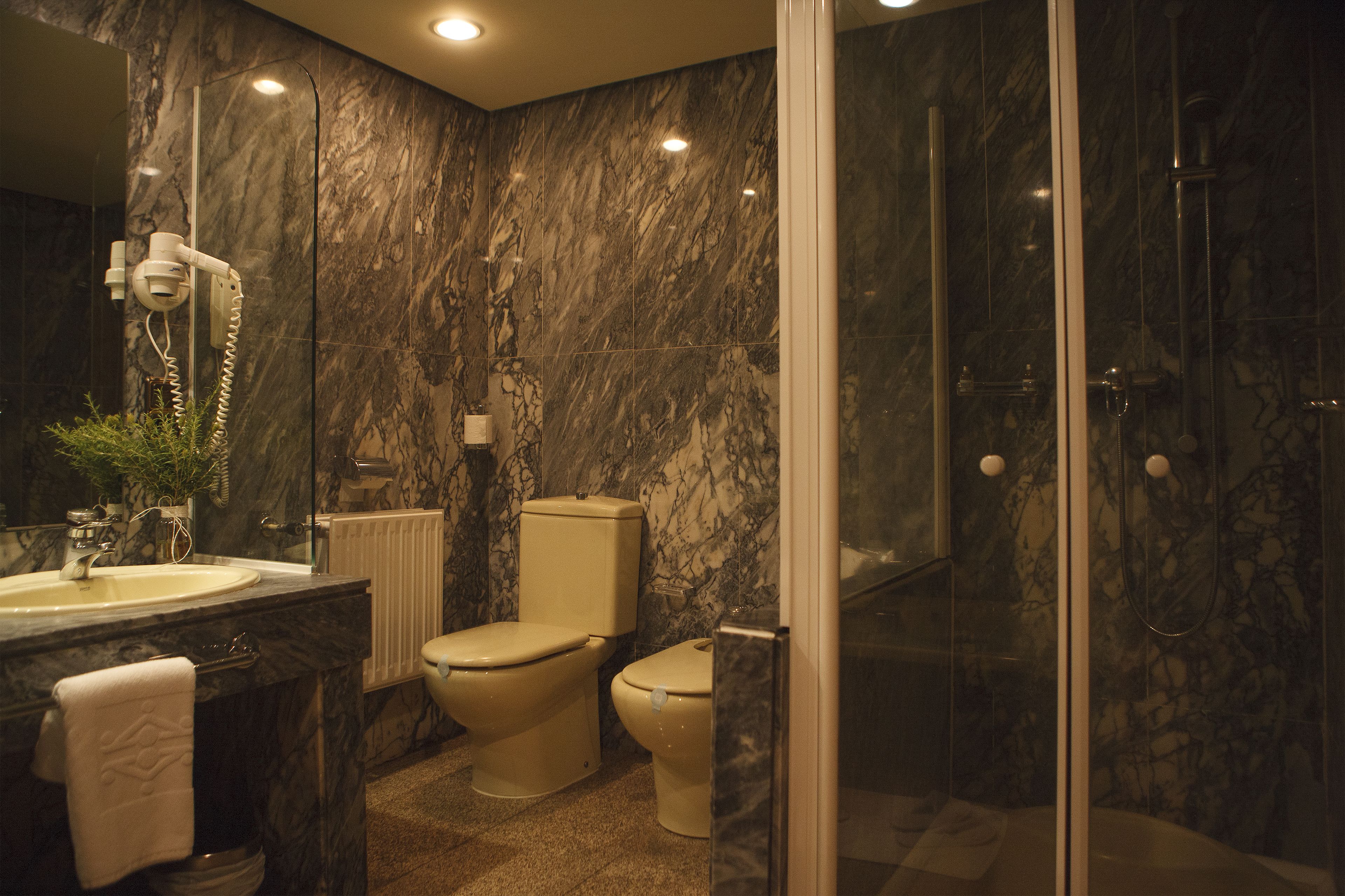 Un baño con pared de mármol, lavamanos, inodoro y zona de ducha.