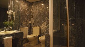 Un baño con pared de mármol, lavamanos, inodoro y zona de ducha.