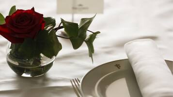 Una mesa de comedor con mantel blanco, un florero de vidrio transparente con una rosa roja y una servilleta blanca doblada.