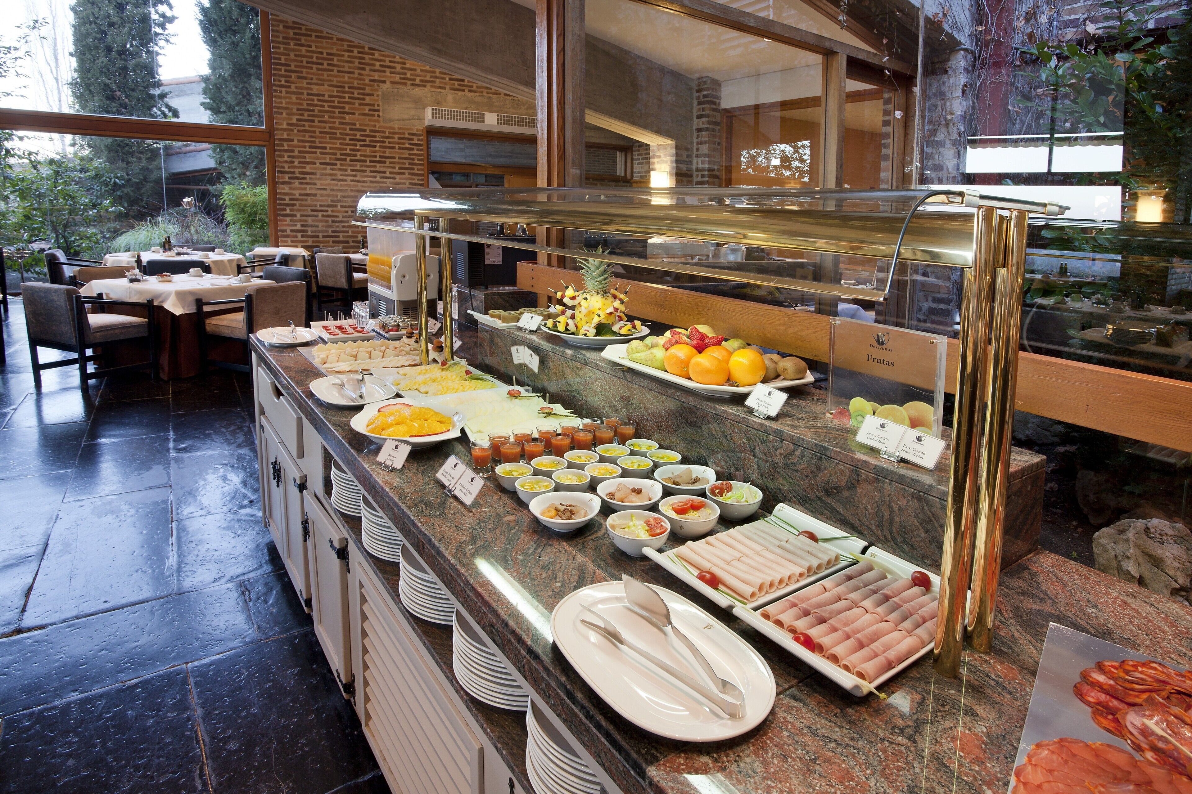 Ein reichhaltiges Buffet mit verschiedenen Speisen, darunter Obst, Fleisch und Salate, in einem hellen Innenbereich mit Blick ins Freie.
