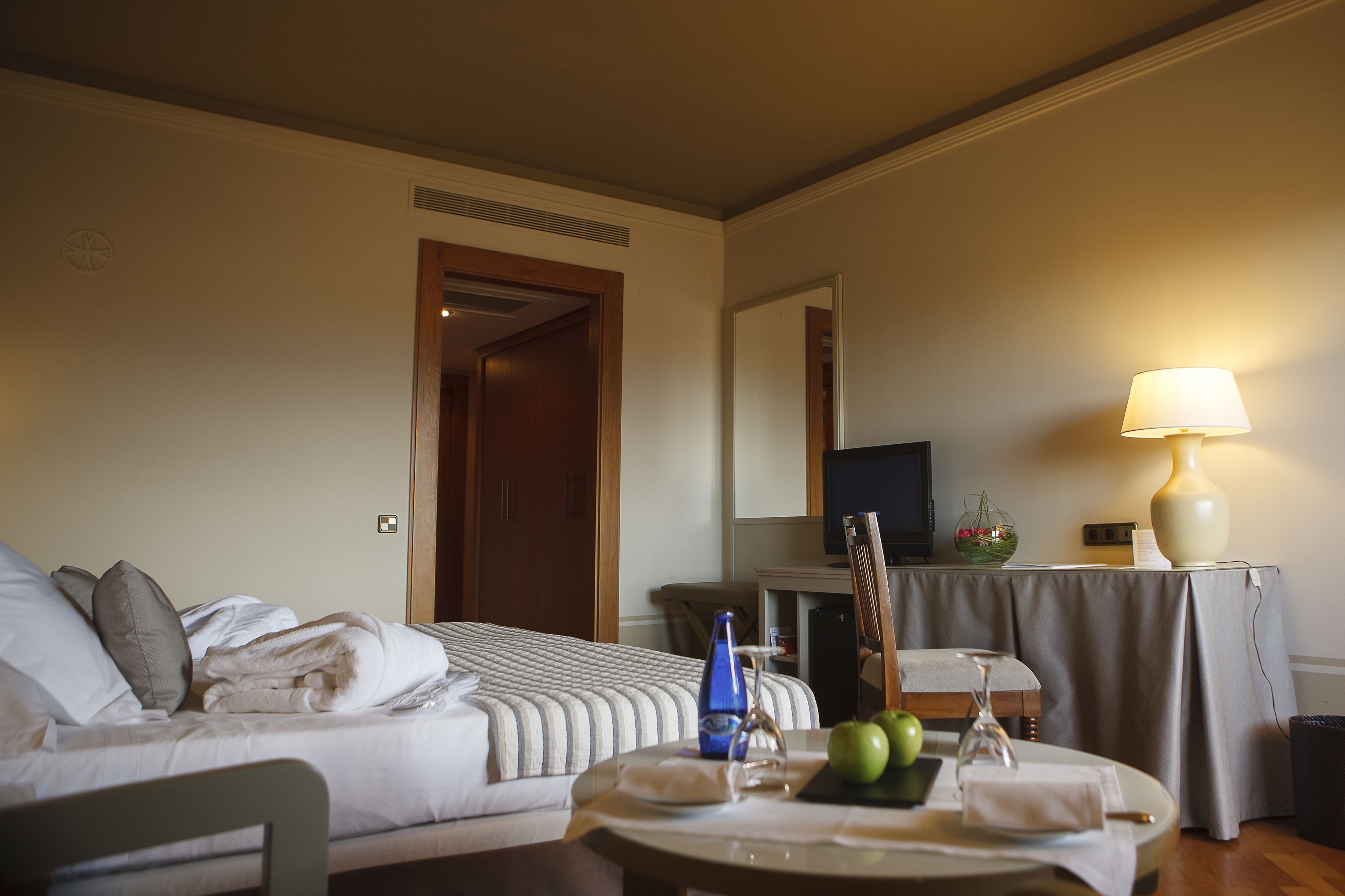 Una habitación de hotel con una cama, una mesa con una lámpara, un televisor y una mesita con un bol y manzanas.